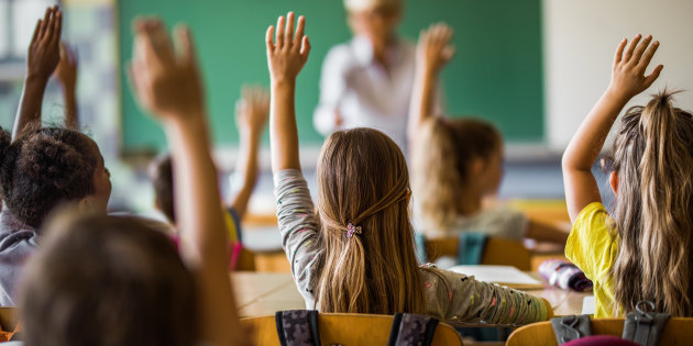 Rear view of large group of students raising their arms to answer the question on a class at elementary school.